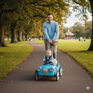 A parent using the adjustable chrome push handle to guide a toddler in a blue ride-on car through a British park.