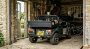 A green two seat electric buggy parked neatly inside a traditional British stone garage alongside gardening equipment.