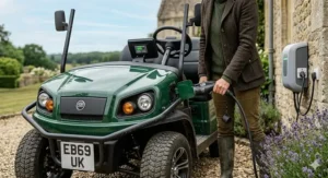 A person plugging a charging cable into a two seat electric buggy using a standard UK wall-mounted power socket.