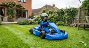 Alt text for image 4: A young child driving a blue 12v ride-on go-kart on a mown grass lawn in a typical British back garden.