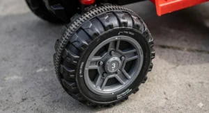 Close-up photorealistic illustration of a chunky all-terrain rubber tyre on a 6v toddler quad bike with an integrated max speed indicator on the wheel hub.