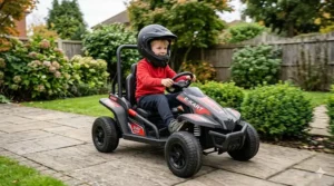 A child wearing a full-face safety helmet racing a red and black 24v electric go kart along a paved garden path.