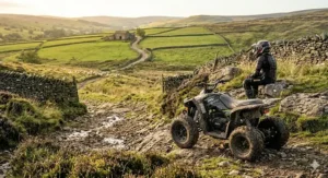 A rider taking a break sitting on a rock next to their 24v quad bike with a backdrop of green hills and traditional dry stone walls.
