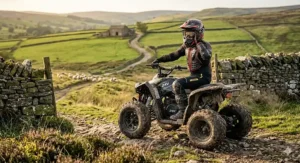 A teenager wearing full safety gear and a helmet riding a red 24v electric quad bike along a winding farm track.