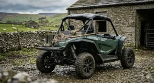 A green electric utility buggy with heavy-duty suspension parked next to a stone barn on a UK farm.