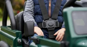 A macro close-up of a 5-point safety harness with textured black webbing buckled securely over a child's jumper inside a ride-on buggy.