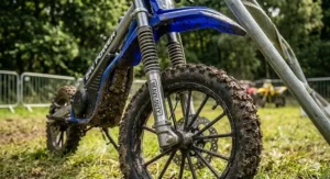 Close-up view of the heavy-duty front suspension and mud-covered knobbly tyres on a 24v electric dirt bike.