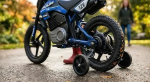 A close-up, photorealistic view of the electric motor housing, battery case, and rear stabiliser wheels of a child's electric motorbike, showing detailed textures on the metal, plastic, and wet rubber.