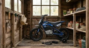 A compact children’s electric motorbike with stabilisers stored safely inside a tidy traditional timber garden shed.