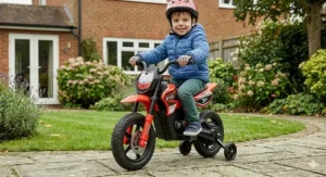 A 3-year-old sitting confidently on an electric motorbike with stabilisers fitted, ready for outdoor play.