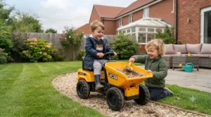 Kids playing together on a sunny day in the UK, using a JCB ride-on dumper to transport sand in a backyard pit.