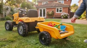 A yellow JCB ride-on tractor equipped with a large detachable trailer filled with plastic garden toys and sand.