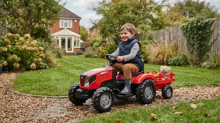 A young boy drives a red 12V kids' ride-on tractor with a trailer in a British garden. kids ride on tractor 12v