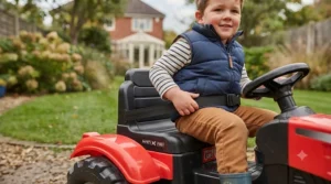 A child securely fastened with a seat belt in the seat of the red 12V kids' ride-on tractor.