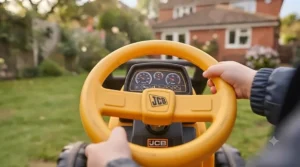 Young child having fun riding a JCB ride-on tractor across the grass in a British back garden during summer.