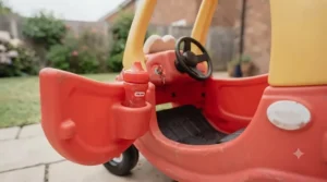 Open driver's side door of the classic red Little Tikes Cozy Coupe with rear cup holders visible for toddler drinks.