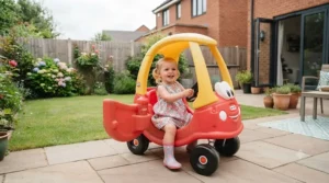 Toddler having fun driving the classic red Little Tikes Cozy Coupe outdoors in a typical British back garden.