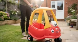 Parent pushing a toddler inside a licensed character Cozy Coupe with the removable floorboard lifted for foot-to-floor motion.