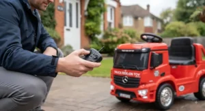 Parent using a safety remote control alongside a ride-on toy truck on a paved driveway