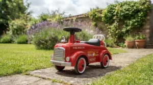 Young boy playing outdoors in a garden with his red fire engine ride-on toy on a sunny day.