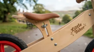 Detail shot showing the height-adjustable padded saddle on a premium wooden balance bike with a brake.