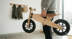 A parent easily carrying a lightweight wooden balance bike by its built-in frame handle after a park session.