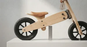 A two-year-old child standing next to an adjustable wooden balance bike to demonstrate correct sizing and seat height.