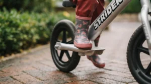 Close-up of a child's feet resting securely on the built-in footrest platform of a Strider balance bike while coasting.